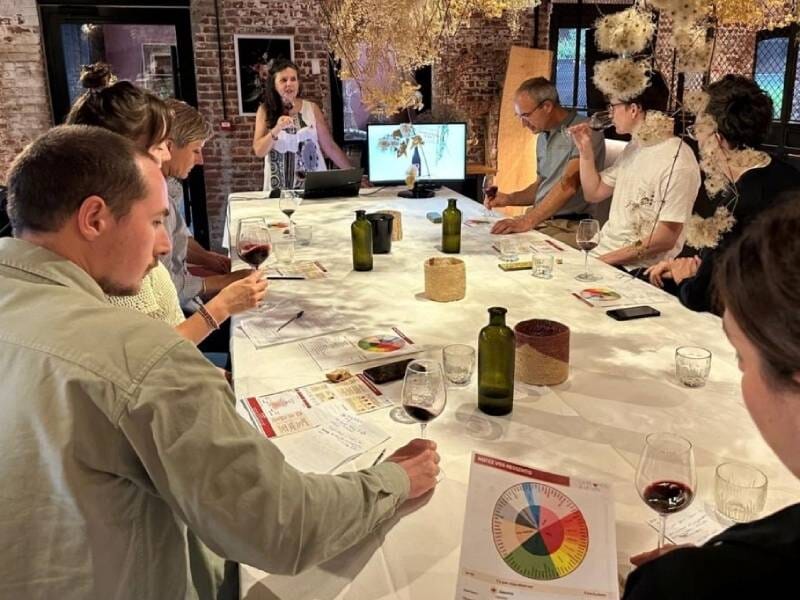 Un groupe de personnes assises autour d'une table participent à un atelier de dégustation de vin avec explications.