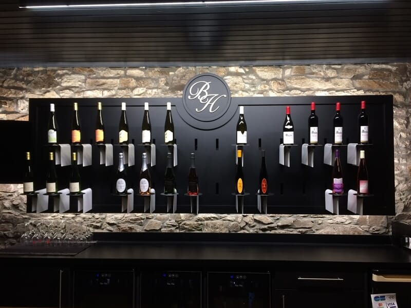 Mur en pierre avec une étagère noire affichant plusieurs bouteilles de vin alignées lors d'un cours d'oenologie près de Cholet.