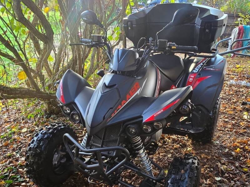 Quad noir et rouge garé sur un sol couvert de feuilles mortes sous des arbres en automne.