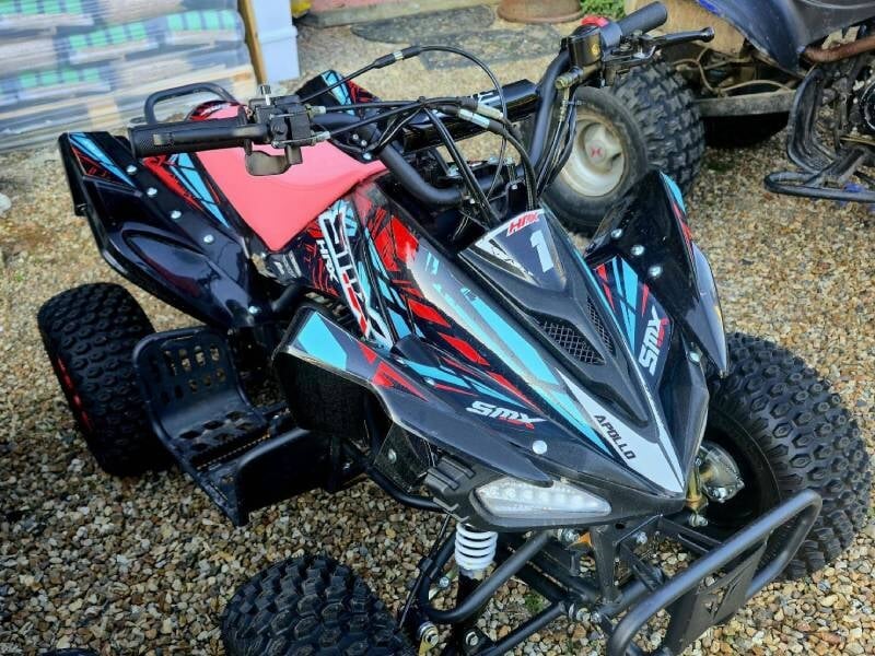 Petit quad sportif noir et rouge avec motifs colorés garé sur un sol en gravier, pour une initiation au pilotage pour enfant près de Tours.
