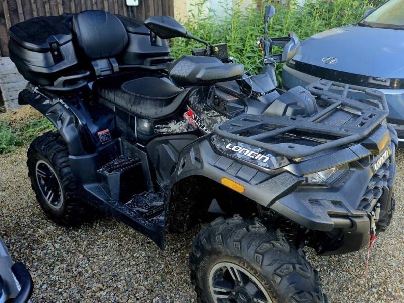 Quad noir avec siège arrière confortable garé sur un sol en gravier.