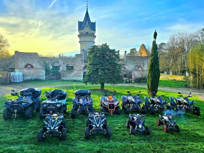 Groupe de quads de différentes tailles et couleurs alignés sur une pelouse devant un château ancien, prêts pour une randonnée près de Tours.