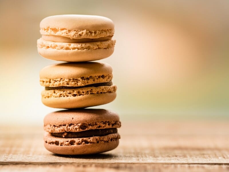 Trois macarons empilés sur une surface en bois, avec un fond flou aux tons chauds et doux.