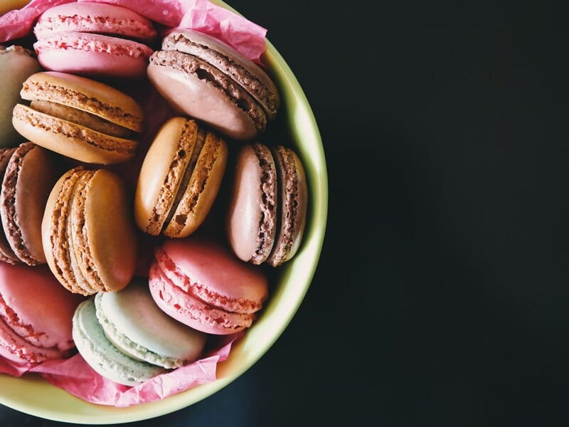 Assiette verte remplie de macarons multicolores posés sur un papier rose, fond noir contrasté.