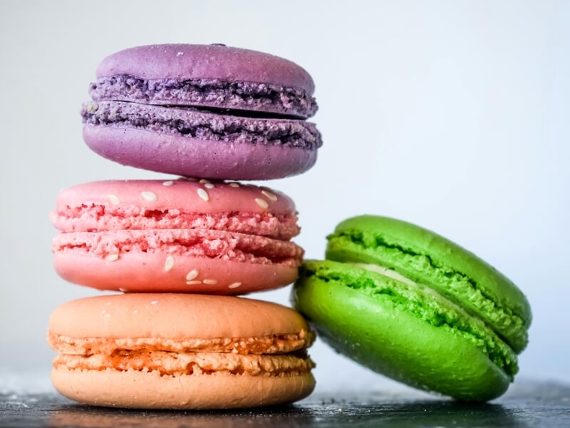 Quatre macarons empilés en diagonale, aux couleurs violet, rose, orange et vert, sur fond clair.