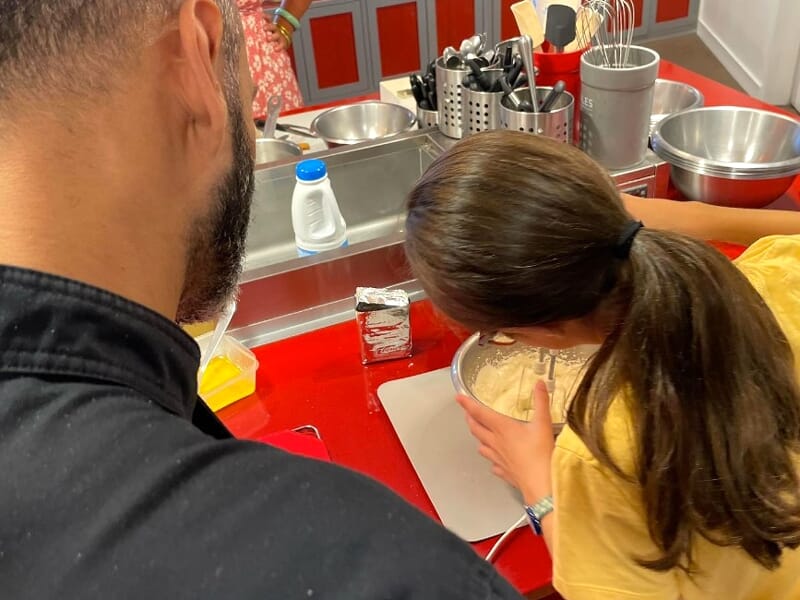 Un homme et une femme en cuisine, la femme mélange une préparation dans un bol sur un plan de travail rouge.