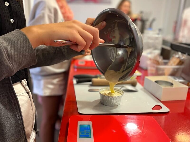 Une personne verse une préparation jaune dans un petit moule rond sur un plan de travail rouge en cuisine.