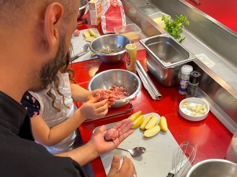 Un homme montre à une enfant comment former des boulettes de viande sur un plan de travail avec divers ingrédients.