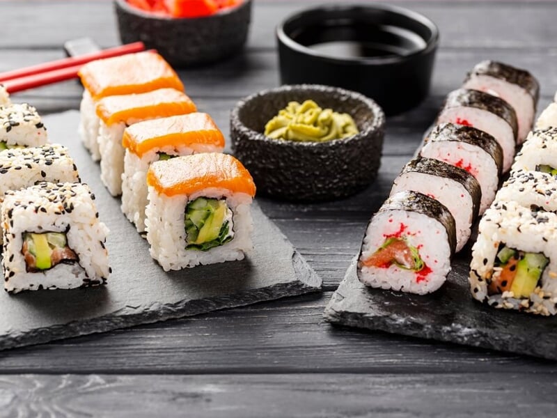Assortiment de sushis variés présentés sur des ardoises noires avec sauce soja et wasabi en accompagnement.