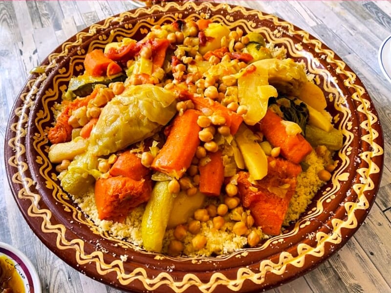 Grand plat de couscous aux légumes variés et pois chiches, présenté dans un plat traditionnel coloré.