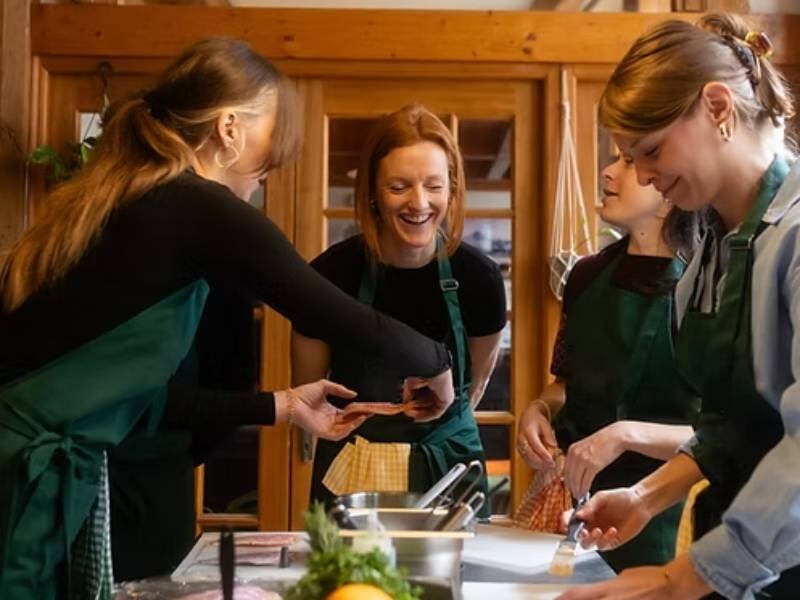 Groupe de quatre personnes souriantes portant des tabliers verts, en train de préparer un plat pendant un cours de cuisine, à Lyon.