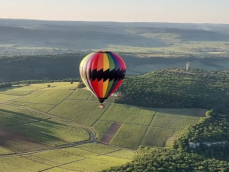 Montgolfière colorée volant au-dessus de collines et vignobles sous un ciel clair au lever du jour