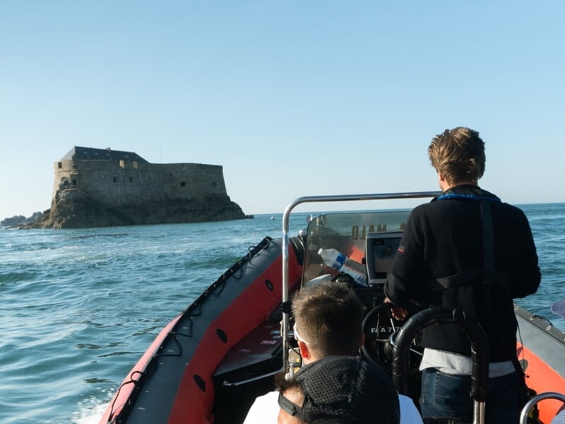 Deux personnes à bord d'un bateau pneumatique approchent d'un fort en pierre lors d'une balade en bateau à Saint-Malo. 