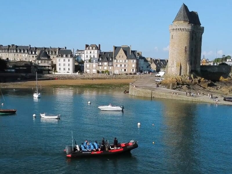 Un bateau pneumatique avec des passagers navigue près d'une tour médiévale lors d'une balade en bateau à Saint-Malo. 