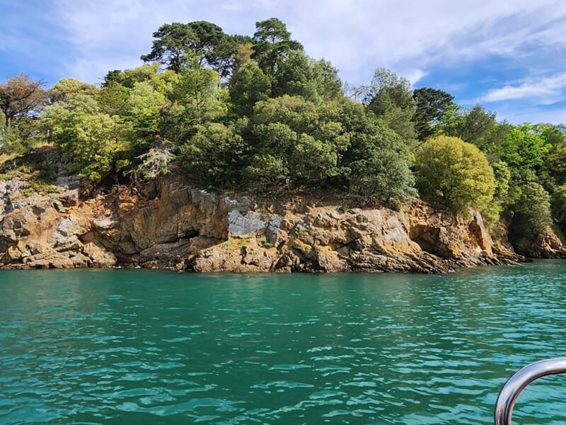 Une côte rocheuse couverte d'arbres verts bordant une mer turquoise lors d'une balade en bateau à Saint-Malo. 