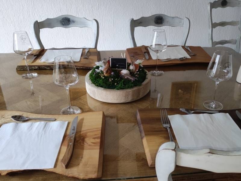 Table en bois dressée avec verres à vin, assiettes et décoration florale au centre dans une salle à manger.