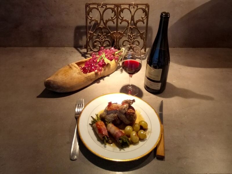 Assiette de viande avec pommes de terre, verre de vin rouge, bouteille de vin et pain décoré de fleurs sur table