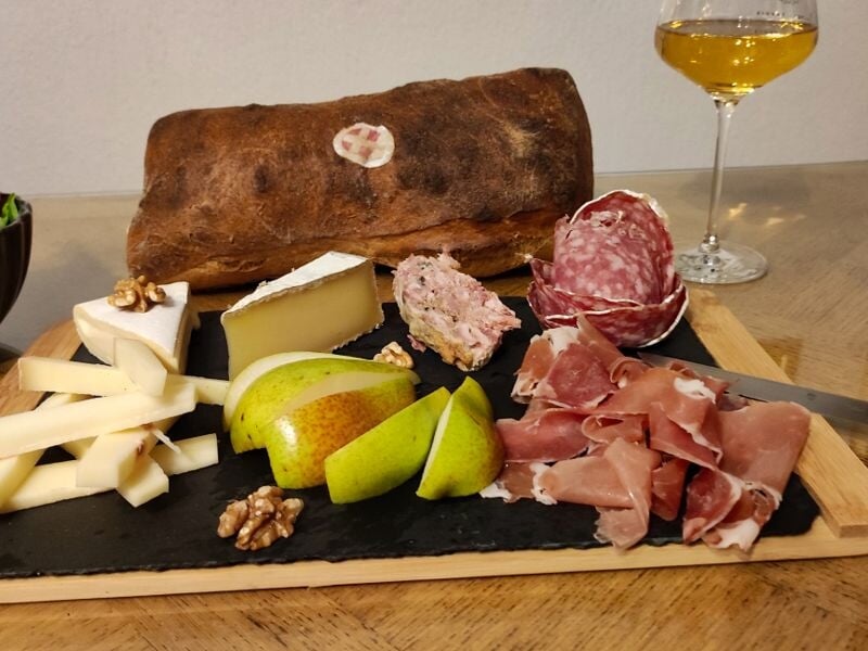Planche de charcuterie, fromages, poires et noix avec verre de vin blanc et pain rustique sur table en bois