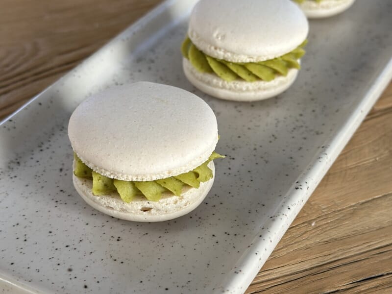 Macarons blancs garnis d'une crème verte, présentés sur un plateau blanc lors d'un cours de pâtisserie à Lille.