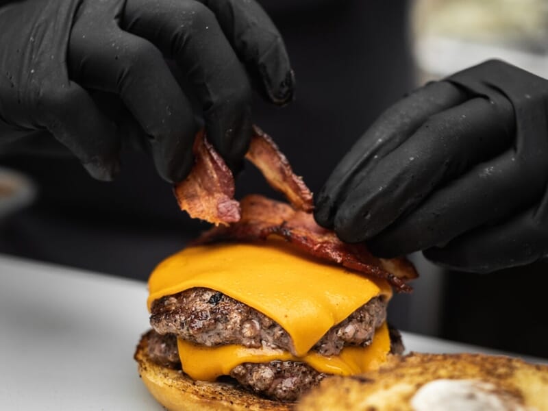 Un chef place des tranches de bacon croustillant sur un double cheeseburger lors d'un cours de cuisine à Lille.