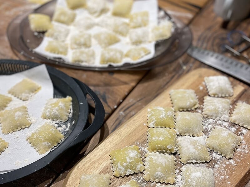 Des raviolis frais faits maison saupoudrés de farine, disposés sur des plateaux en bois et en métal, lors d'un cours de cuisine à Lille.