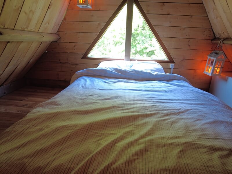 Chambre mansardée avec un grand lit double sous une fenêtre triangulaire lors d'une nuit cabane près de Saint-Nazaire.