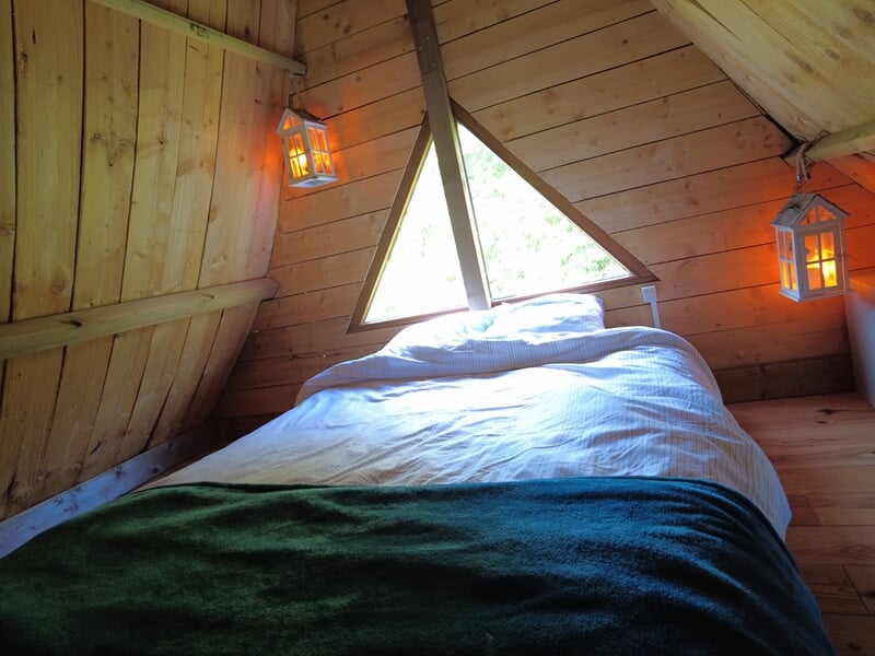 Chambre mansardée avec lit double, couverture verte et deux lanternes lors d'une nuit cabane près de Saint-Nazaire.