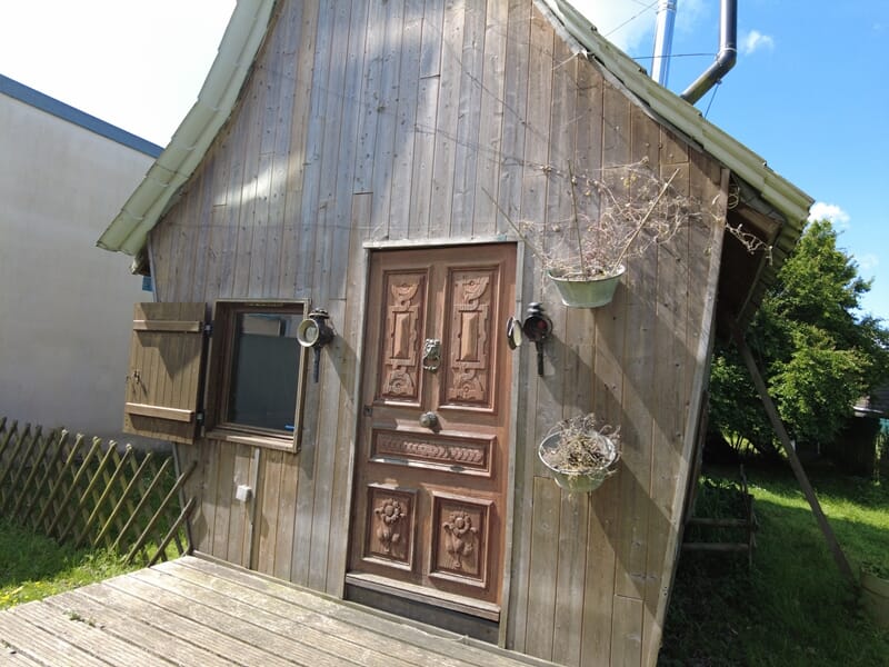 Façade en bois d'une petite maison avec porte sculptée, fenêtre à volets ouverts lors d'une nuit cabane près de Saint-Nazaire.