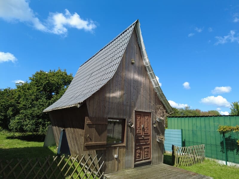 Petite maison en bois avec toit en ardoise, porte sculptée, jardin et ciel bleu lors d'une nuit cabane près de Saint-Nazaire.
