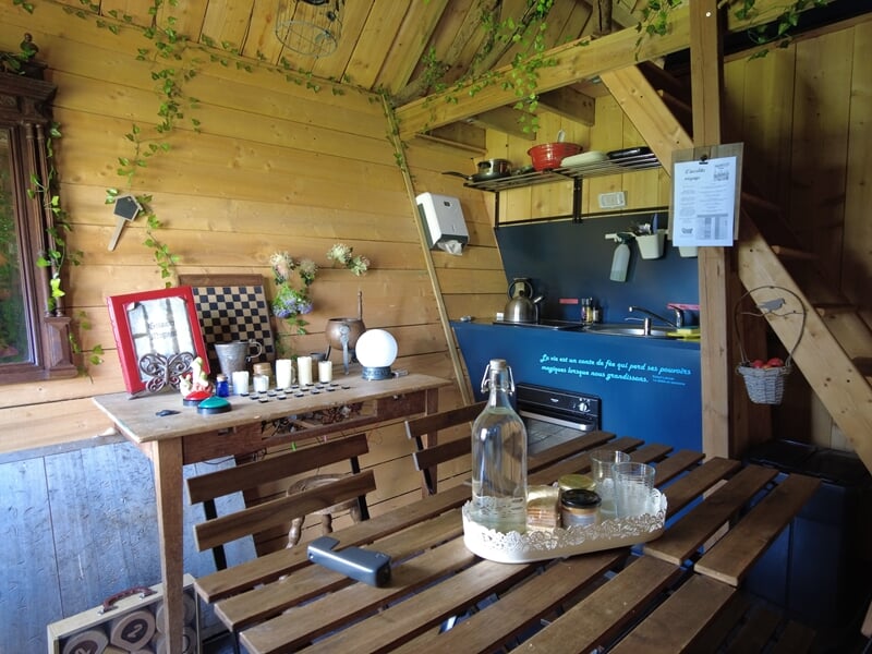 Coin repas avec table en bois, bouteille d'eau, verres, et cuisine équipée lors d'une nuit cabane près de Saint-Nazaire.