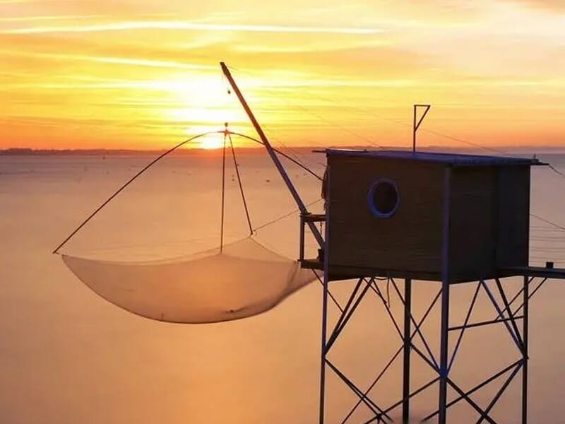Cabane de pêche sur pilotis avec filet carré suspendu au-dessus de l'eau au coucher du soleil, lors d'une location pêche à Saint-Nazaire.