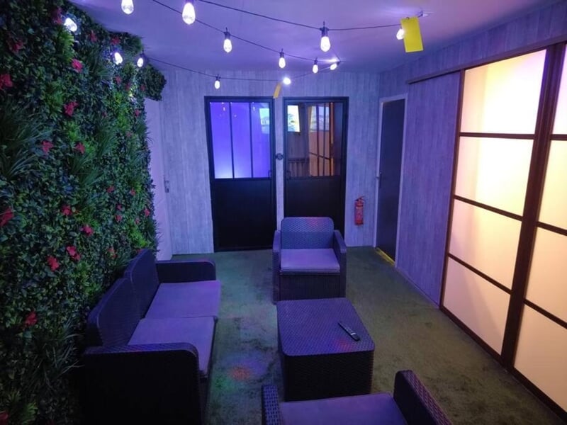 Salon avec canapé et fauteuils noirs, table basse, mur végétal lors d'une nuit en Love Room près de Châteauroux.