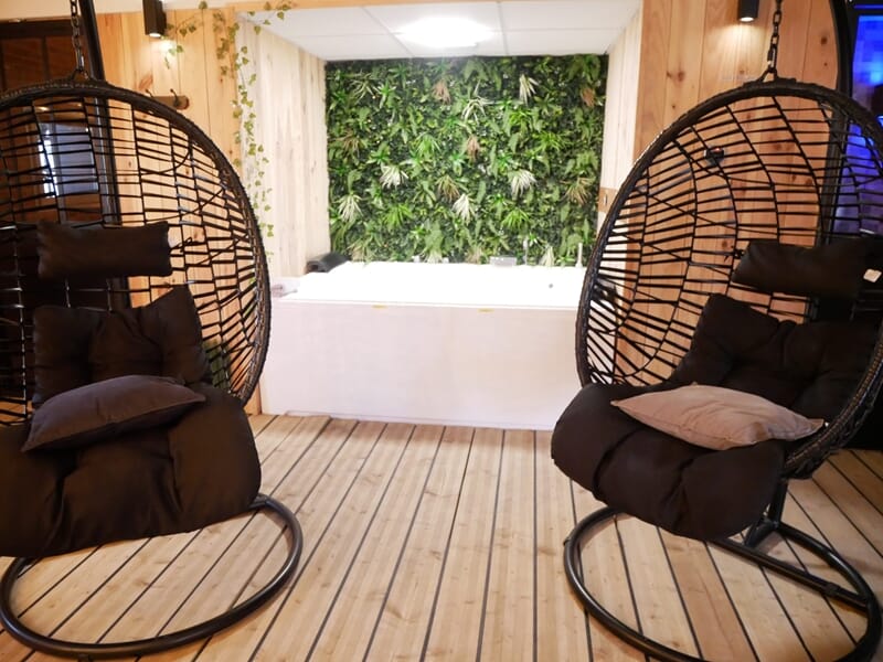 Deux fauteuils suspendus noirs avec coussins, jacuzzi blanc et mur végétal lors d'une nuit en Love Room près de Bourges.