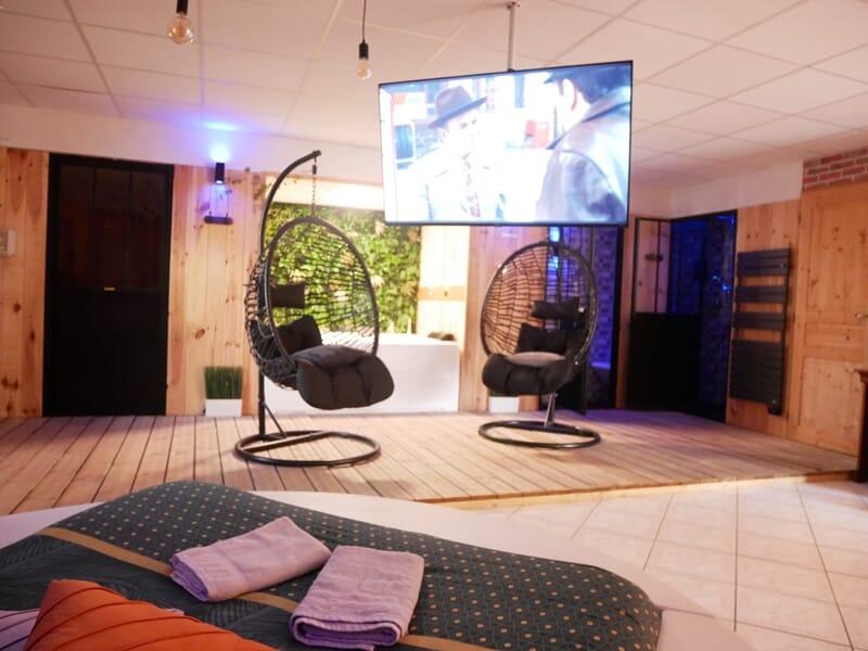 Vue d'ensemble d'une pièce avec lit rond, fauteuils suspendus, jacuzzi, lors d'une nuit en Love Room près de Bourges.