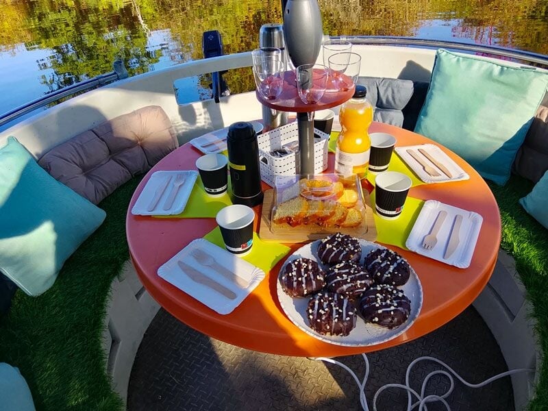 Table ronde sur un bateau avec des assiettes, verres, jus d'orange et biscuits au chocolat pour un repas convivial.
