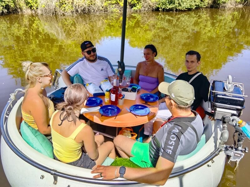 Groupe de six personnes assises autour d'une table ronde sur un bateau, profitant d'un moment convivial.
