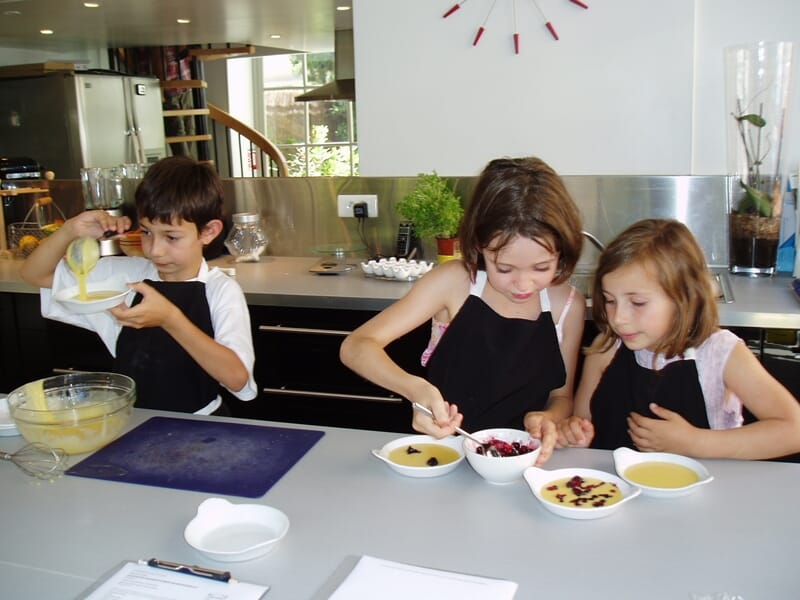 Trois enfants en tabliers noirs préparent des desserts lors d'un cours de cuisine à Nice. 