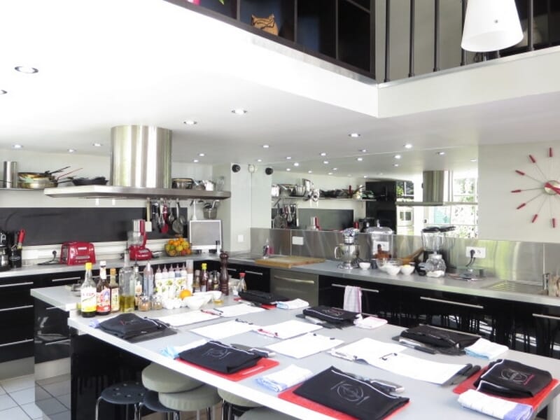 Salle de cours de cuisine avec tables dressées, tabourets, et équipements culinaires lors d'un cours de cuisine à Nice. 