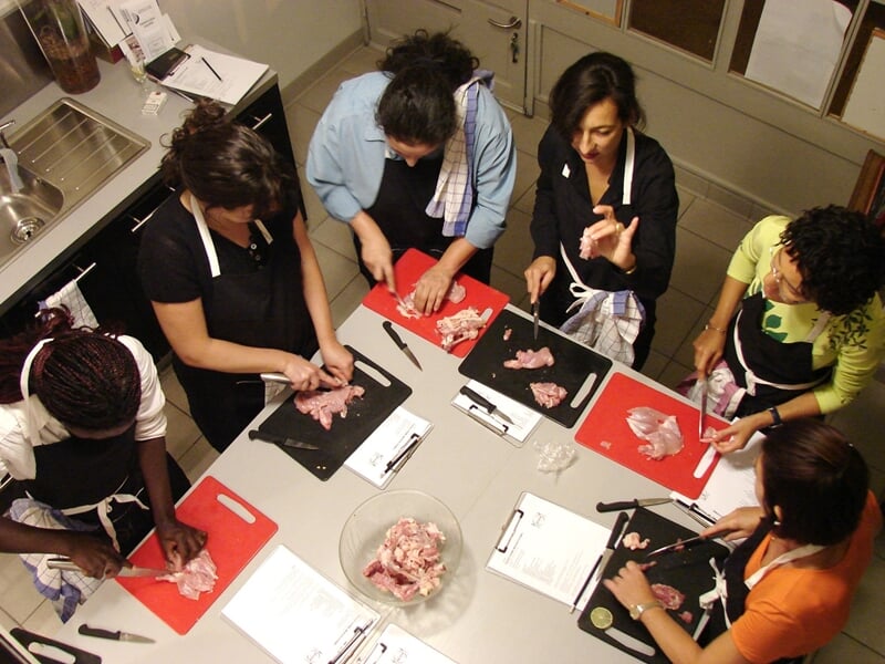 Groupe de six personnes apprenant à découper de la viande lors d'un cours de cuisine à Nice.
