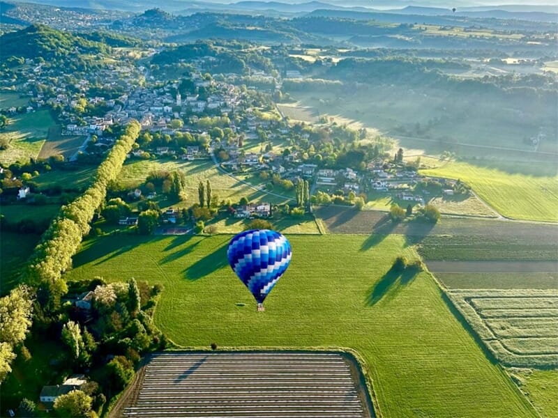Vue aérienne d'une montgolfière bleue survolant des champs verts lors d'un vol en montgolfière près de la Montagne de Lure.