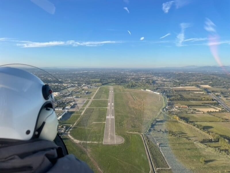 Pilote dans un ULM survolant une piste d'atterrissage entourée de champs lors d'un vol en ULM autogire près d'Avignon. 