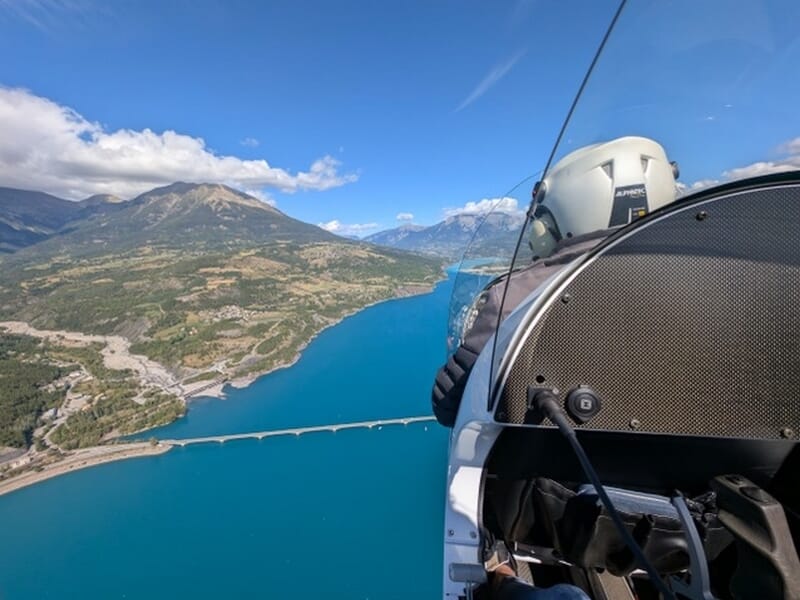 Pilote dans un ULM survolant un lac turquoise lors d'un vol en ULM autogire près d'Avignon. 