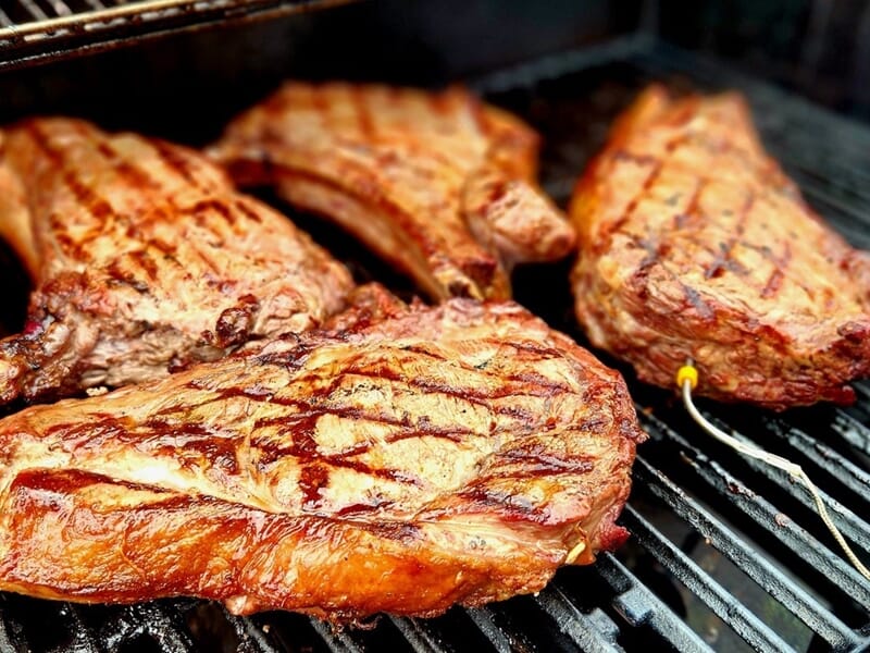 Plusieurs côtes de viande bien grillées avec des marques de cuisson sur un barbecue noir en extérieur.