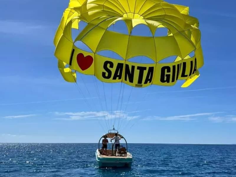 Bateau en mer avec parachute ascensionnel jaune marqué Santa Giulia, ciel bleu et mer calme en arrière-plan.