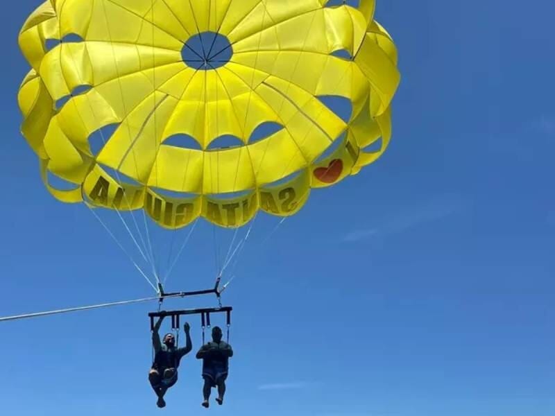Deux personnes en parachute ascensionnel suspendues à un parachute jaune au-dessus de la mer, ciel bleu clair.