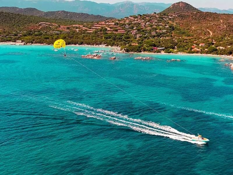 Vue aérienne d'un bateau tirant un parachute ascensionnel jaune au-dessus de l'eau turquoise, lors d'un vol près de Porto-Vecchio.