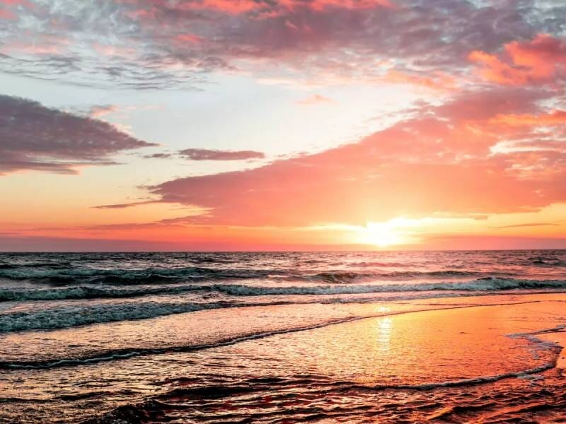 Coucher de soleil sur une plage avec des vagues douces et un ciel aux couleurs chaudes orangées et roses.