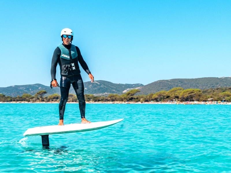 Homme en combinaison et casque sur un e-foil flottant au-dessus de l'eau turquoise de Santa Giulia, près de Porto-Vecchio.