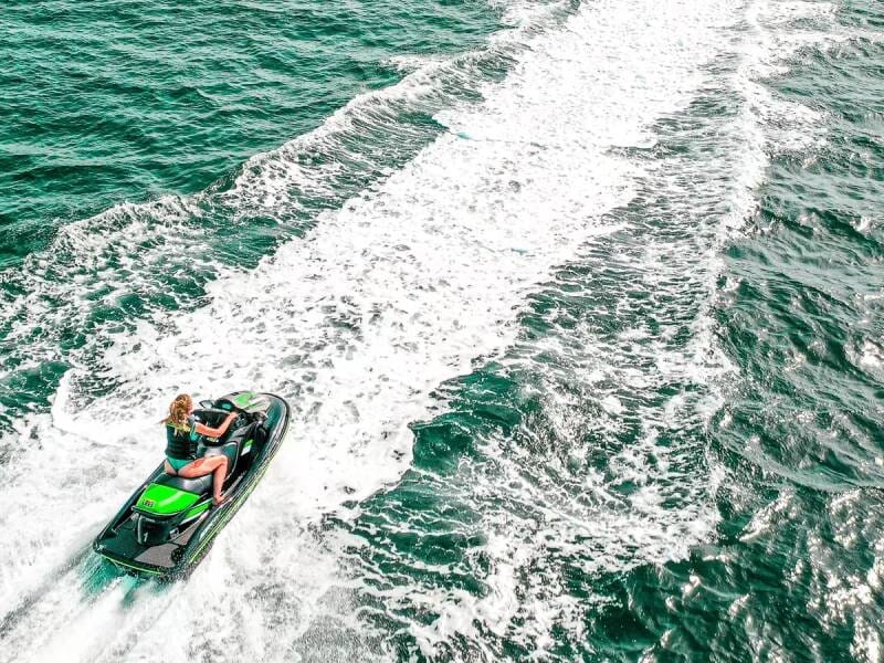 Personne conduisant un jetski vert sur une mer agitée avec une traînée blanche devant et derrière l'appareil.