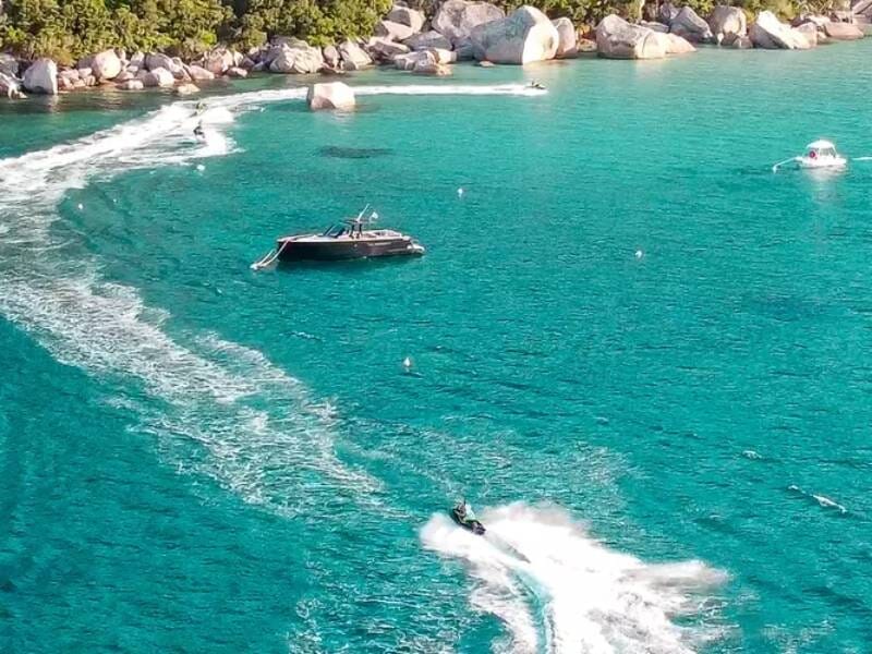 Jetski naviguant dans une eau turquoise claire près d'un bateau noir et d'une côte rocheuse verdoyante.